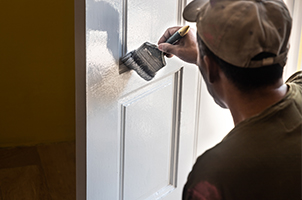 Professional painter applying fresh paint to the front door of a new home, representing a fresh start and customization for the homeowners.