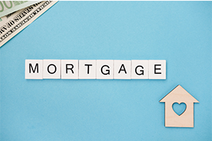 Letters spelling out the word "mortgage" on a table with a house model in the corner.