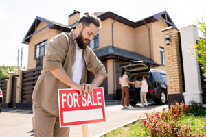 Man placing a For Sale sign in front of a beautiful home on a sunny spring day, illustrating the best month to sell a house.